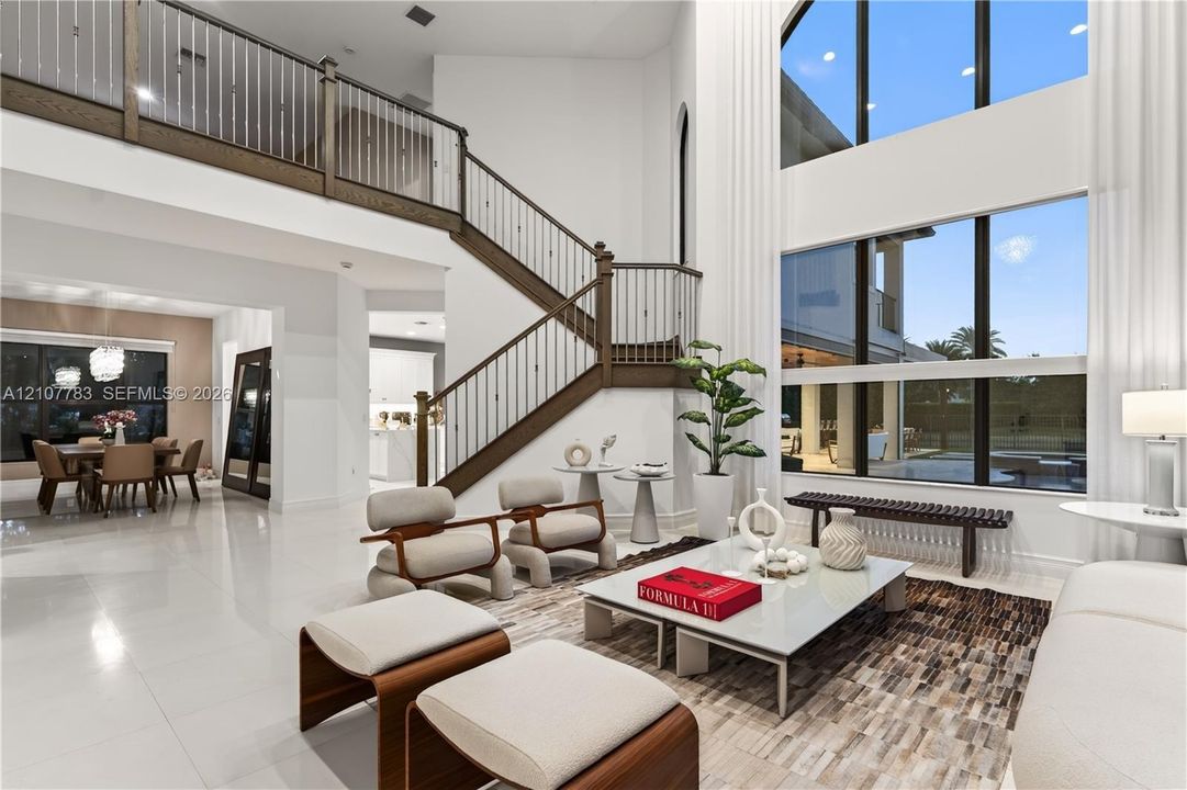Two-story living area featuring floor-to-ceiling windows, porcelain tile flooring, and a grand staircase with wood-finished handrails and metal balusters