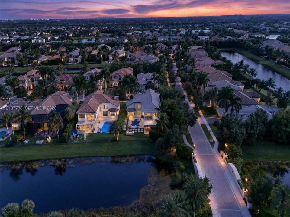 Aerial perspective of a residential neighborhood featuring waterfront lots, paved roadways, mature palm trees, and rear-yard swimming pools