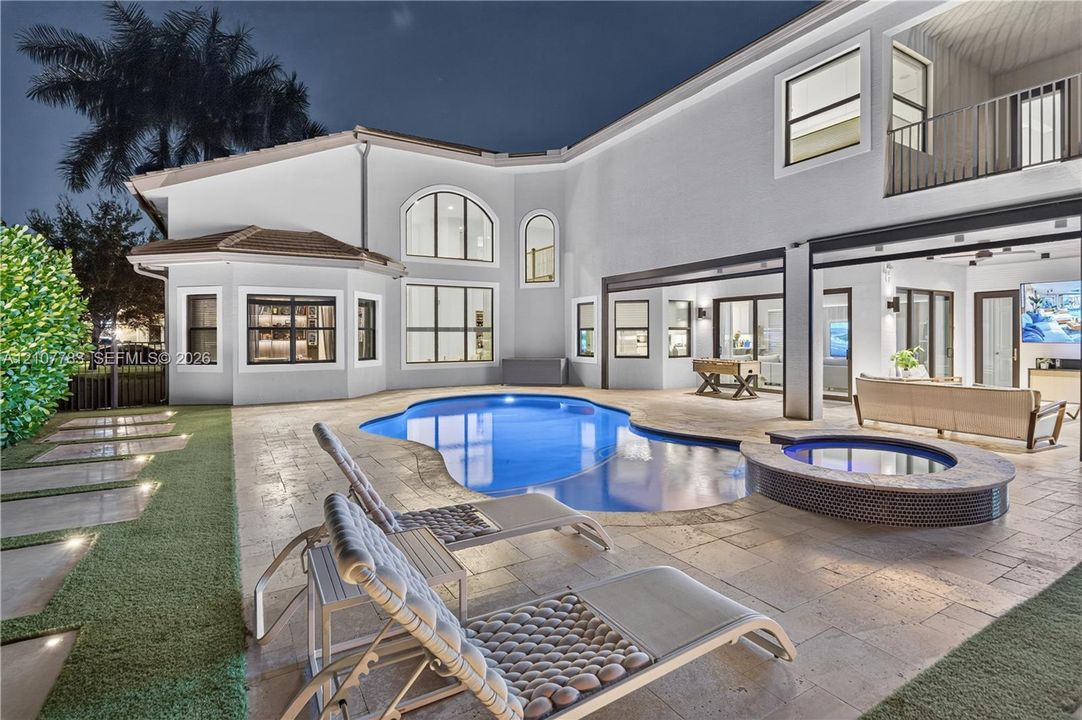 Stucco exterior featuring a resort-style pool, raised spa with tile surround, natural stone paver patio, and covered outdoor living area