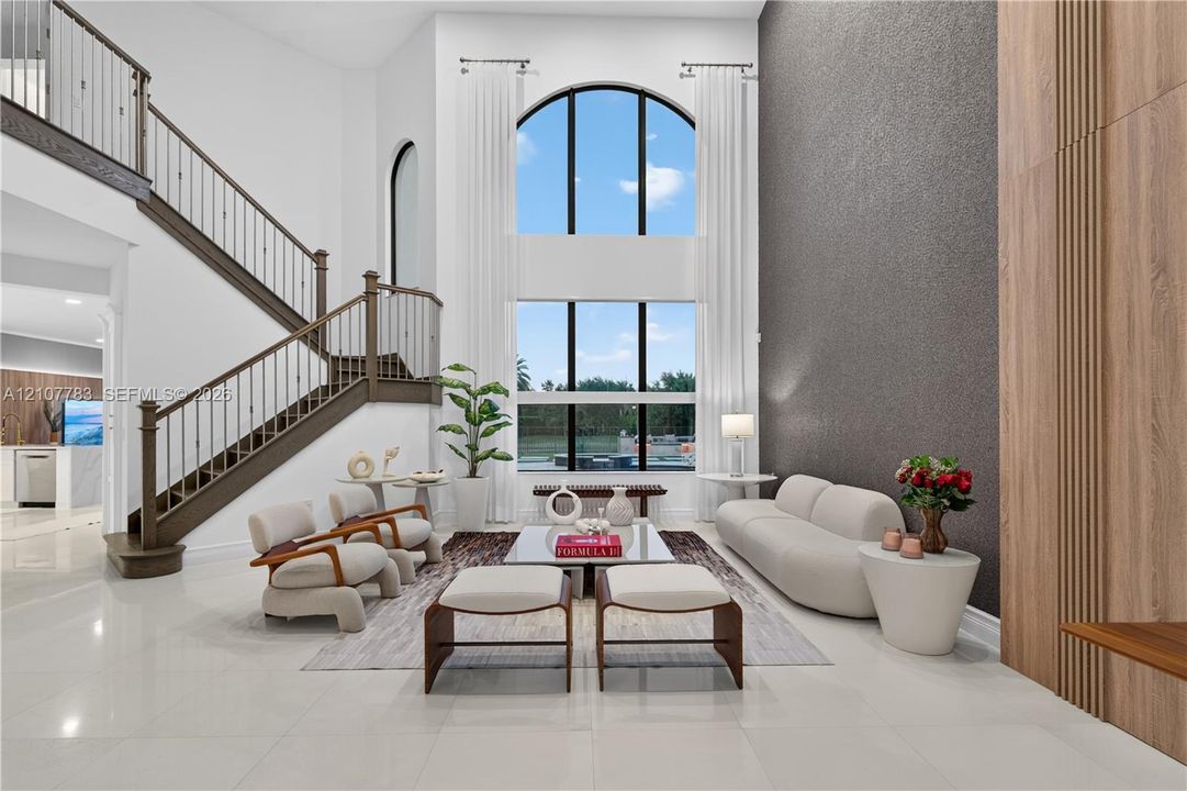 Two-story great room featuring a double-height arched window, floor-to-ceiling textured accent wall, wood-paneled wall detail, and a staircase with wrought iron railing