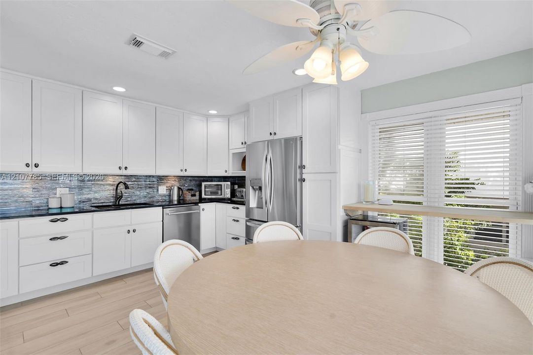 Kitchen featuring white shaker-style cabinetry, dark stone countertops, blue glass tile backsplash, stainless steel appliances, and wood-finish flooring