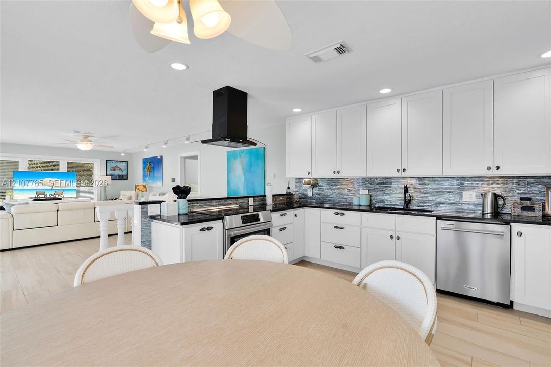 Kitchen featuring white cabinetry, dark countertops, a textured tile backsplash, a stainless steel dishwasher, and a matte black wall-mounted range hood