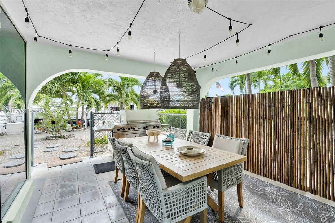 Covered patio featuring ceramic tile flooring, built-in stainless steel outdoor kitchen, arched architectural detailing, and decorative woven pendant lighting