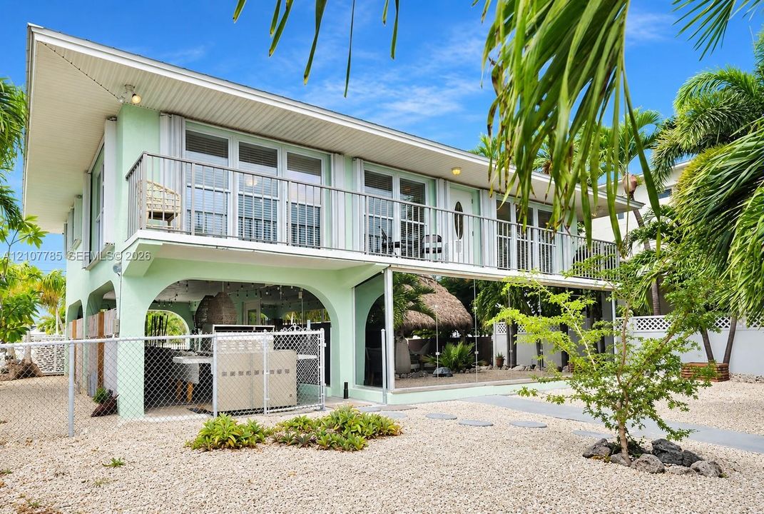 Elevated exterior featuring a second-story balcony with metal railing, ground-level covered patio with arched masonry, and exterior staircase