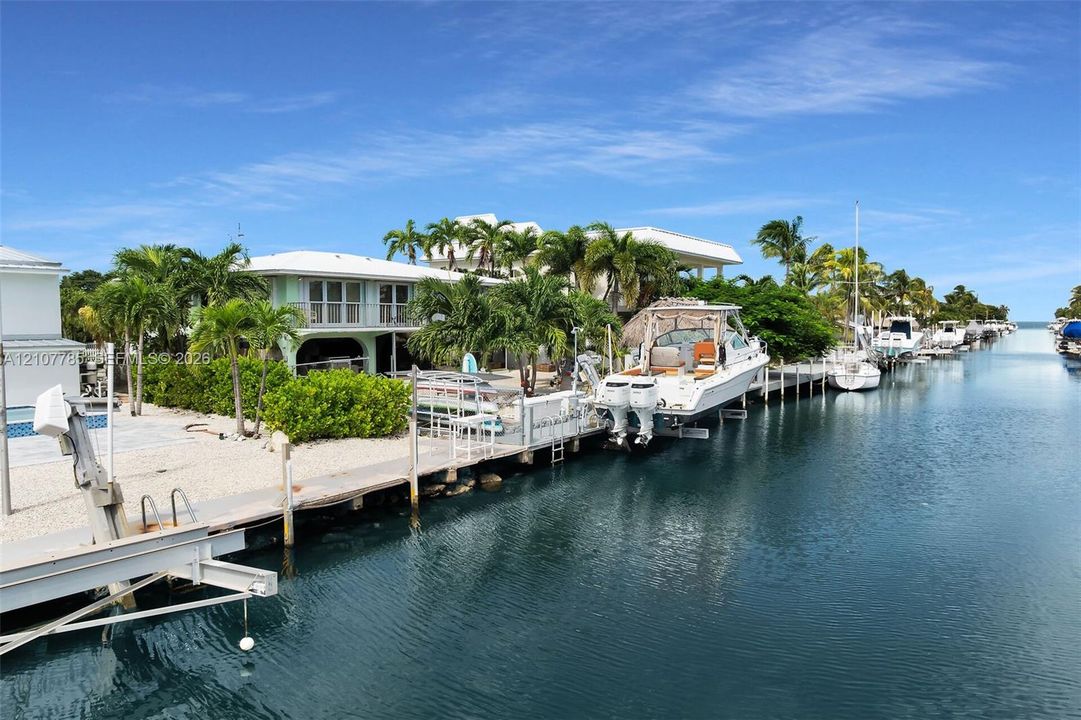 Deep-water canal frontage featuring a private dock, mechanical boat lift, concrete seawall, and mature tropical landscaping