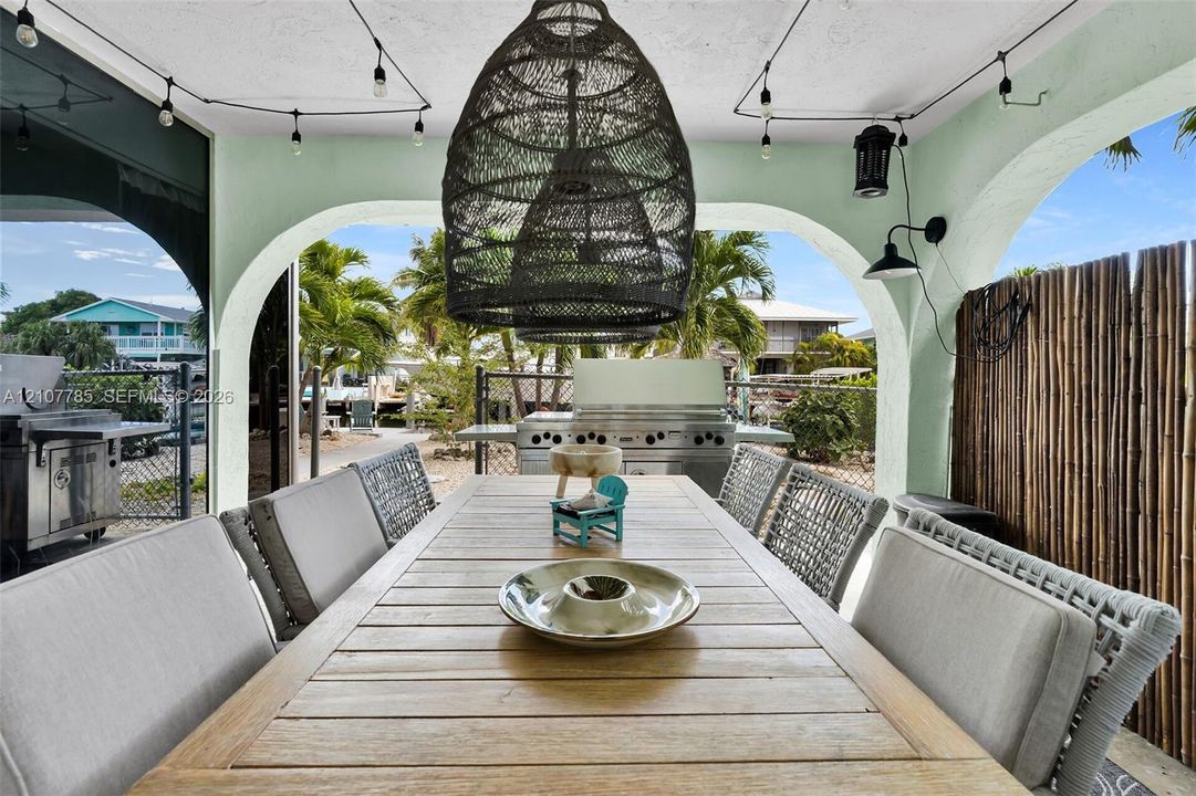 Covered outdoor living space featuring arched structural openings, built-in stainless steel grill, woven pendant light fixture, and mounted exterior wall sconces