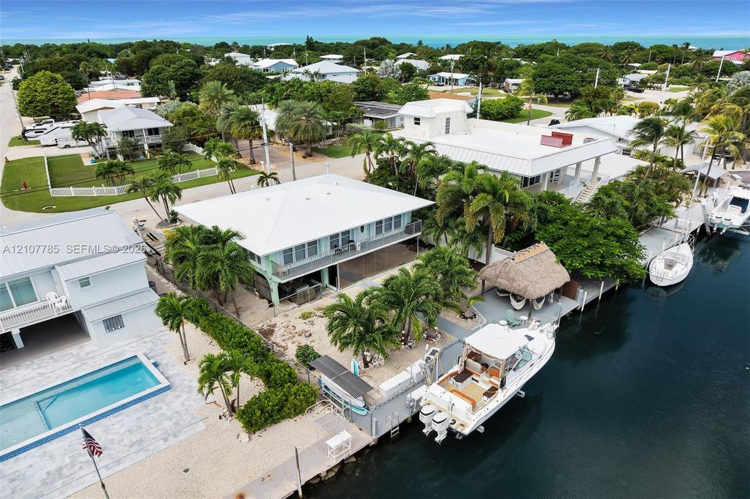 Waterfront property featuring a private boat dock, a thatched-roof tiki hut, mature palm landscaping, and a second-story balcony