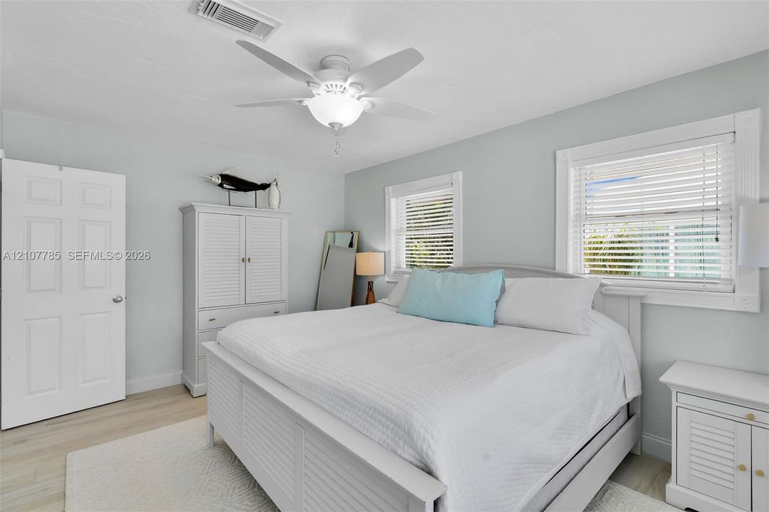 Light-filled room featuring wood-finish flooring, a white ceiling fan with integrated lighting, and dual windows with horizontal blinds