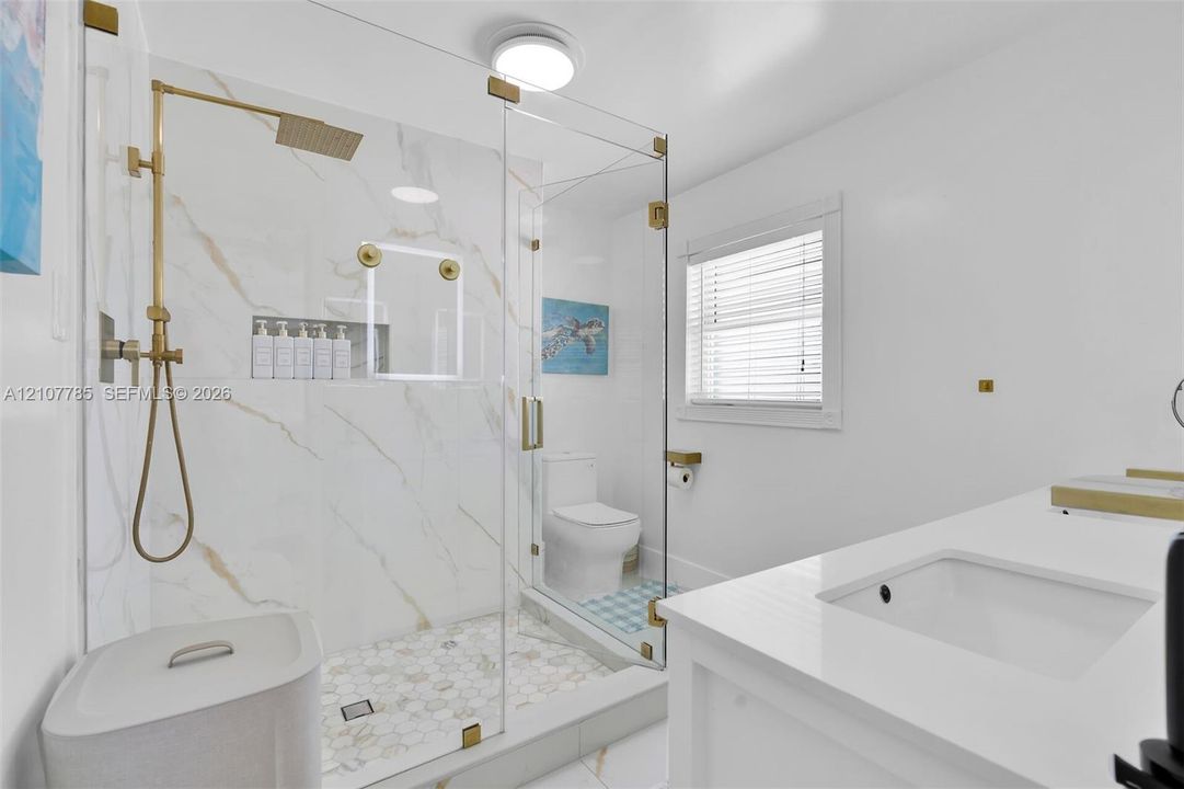Walk-in shower with gold-tone hardware, a built-in recessed niche, stone-finish wall tile, a hexagonal tile floor, and a frameless glass enclosure