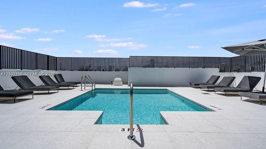 Rooftop pool with tile surround, metal perimeter fencing, and stainless steel handrails