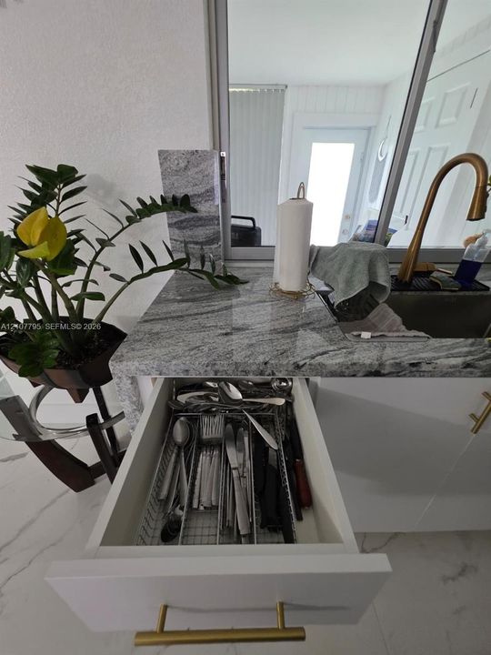 Kitchen sink area featuring stone-finish countertops, white cabinetry with gold-tone hardware, and a high-arc faucet