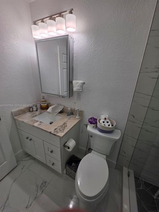 Bathroom featuring a white vanity cabinet, neutral stone-finish countertop with an integrated basin, mirrored medicine cabinet, five-light fixture, and large-format tile flooring