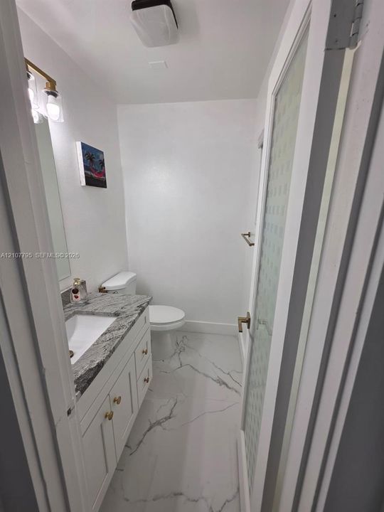 Bathroom featuring a stone-top vanity with built-in cabinetry, large-format tile flooring with marble-style veining, and a door with frosted glass paneling