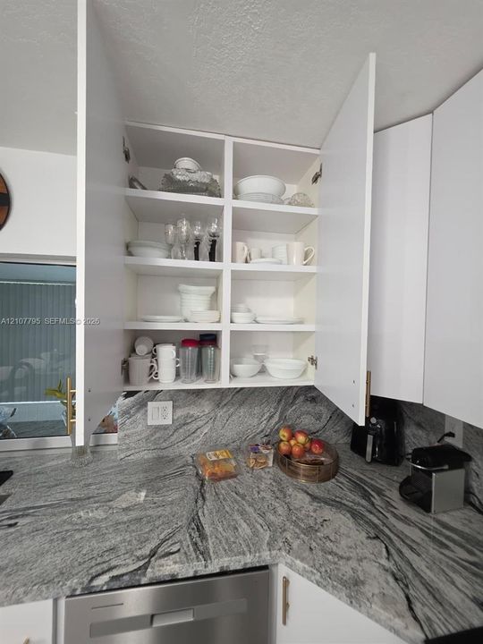 White cabinetry with custom shelving, stone-surfaced countertops, and stainless steel hardware