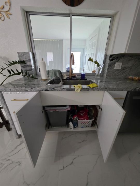 Kitchen sink area featuring stone countertops, white cabinetry with gold-toned hardware, a metallic finish pull-down faucet, and light-toned tile flooring