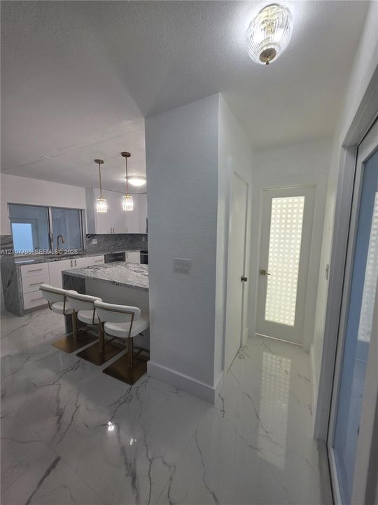 Kitchen featuring a stone-surface island, white cabinetry, light-toned stone-finish flooring, ceiling-mounted pendant lighting, and a door with frosted grid-patterned glass