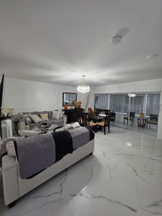Polished stone-finish flooring with neutral veining, multi-pane sliding glass doors, and a decorative crystal-style chandelier