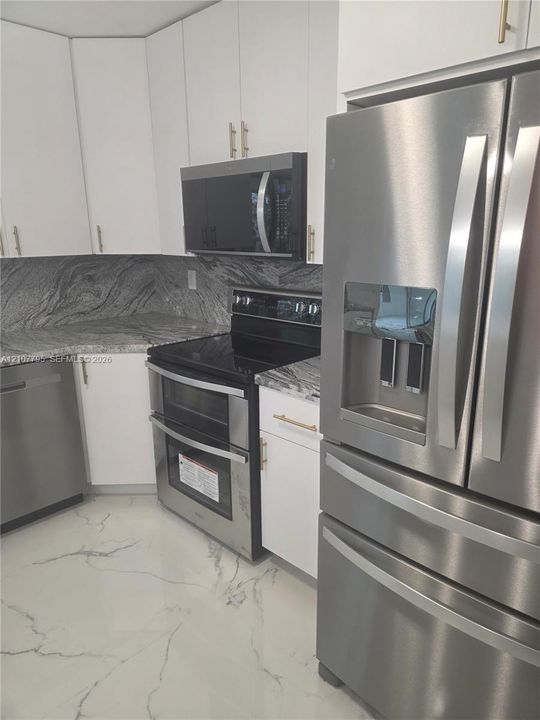 Kitchen featuring white cabinetry with metallic pulls, stone-patterned countertops, a full suite of stainless steel appliances, and large-format tile flooring with veining detail