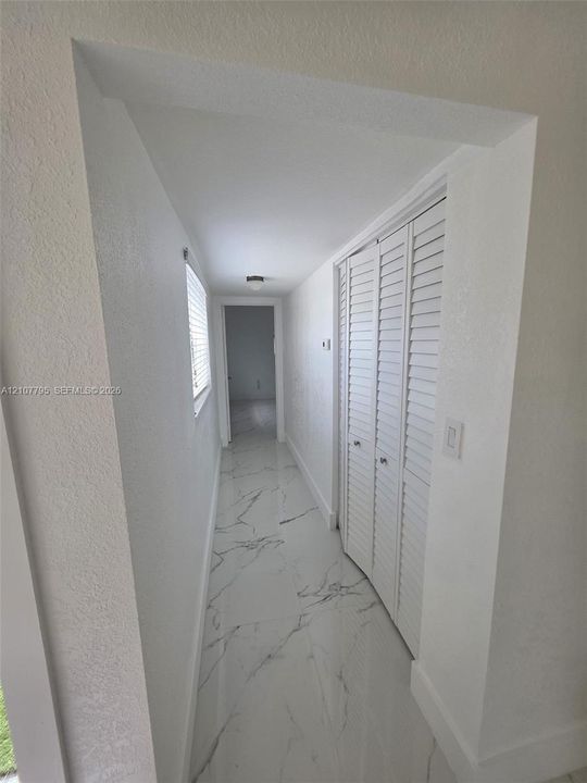 Hallway featuring large-format tile flooring with a veined pattern, louvered bi-fold closet doors, and flush-mount ceiling lighting
