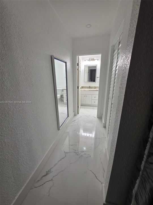 Hallway featuring polished large-format tile flooring with a veined pattern, recessed lighting, and a wall-mounted rectangular mirror