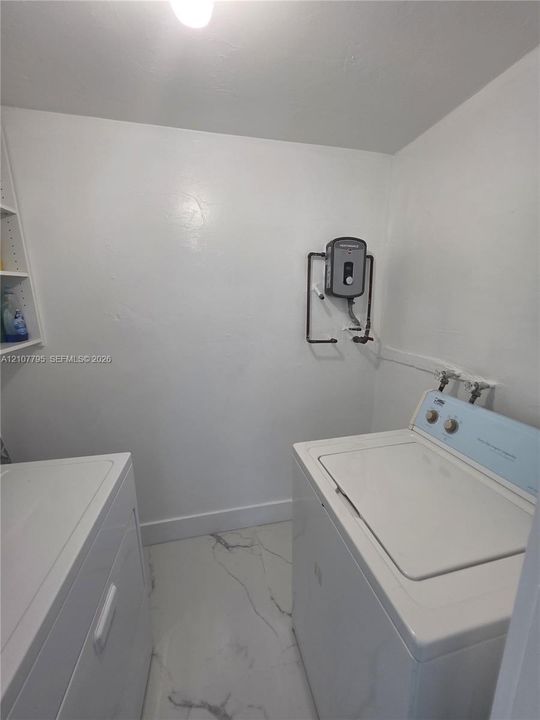 Utility space featuring white stone-finish flooring, wall-mounted tankless water heater, and built-in white shelving