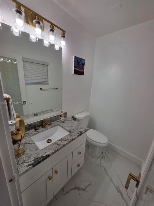 Bathroom vanity featuring a stone countertop, white undermount basin, brushed gold hardware, large-scale wall mirror, and five-light vanity fixture over large-format tile flooring