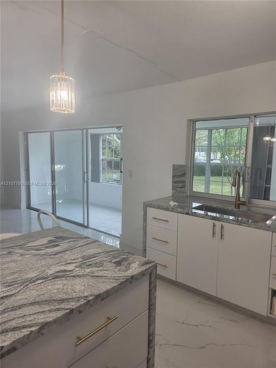 Kitchen featuring stone countertops, white cabinetry with metallic hardware, a stainless steel undermount sink, porcelain tile flooring, and a pendant light fixture