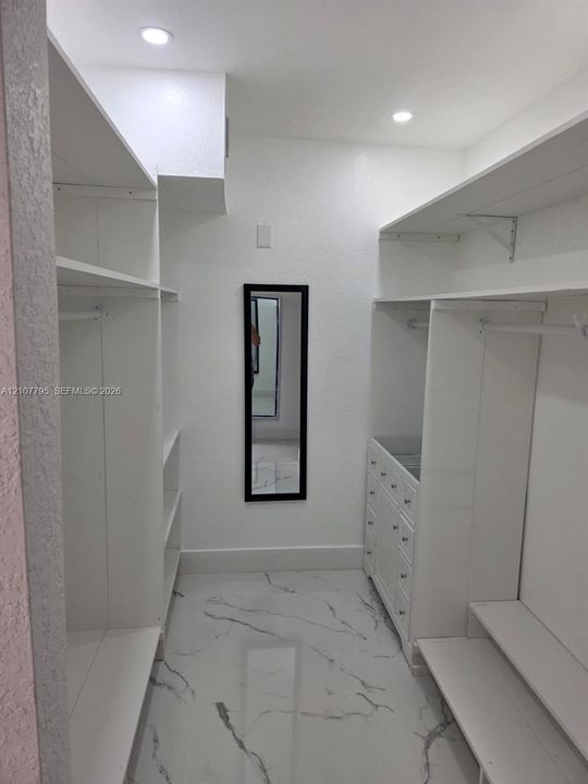 Walk-in closet featuring white built-in shelving, integrated dresser drawers, recessed lighting, and tile flooring with a marble-finish pattern