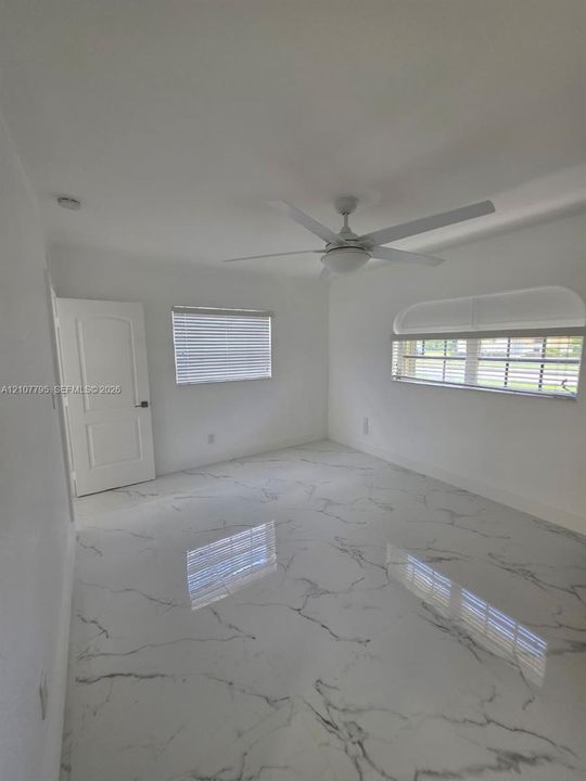 Polished stone-finish flooring with marbled veining, arched window design, white multi-panel interior door, and integrated ceiling fan with light fixture