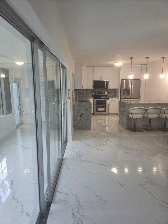 Modern kitchen featuring large-format tile flooring, stone-finish countertops, stainless steel appliances, white flat-panel cabinetry, and floor-to-ceiling glass sliding doors