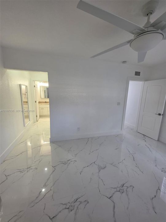 Polished stone-finish flooring with veined detail, ceiling fan with integrated lighting, and solid-core paneled interior door