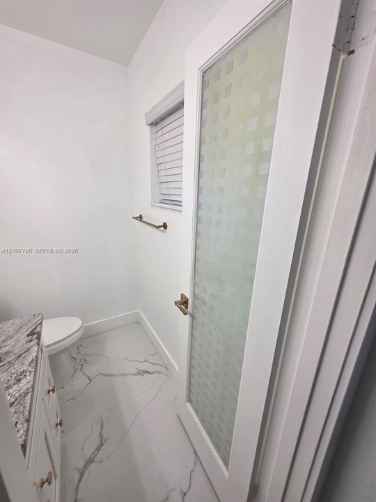 Door featuring a frosted glass panel with a geometric pattern, stone-finish countertop with white cabinetry, light-toned stone-finish flooring, and metallic hardware fixtures