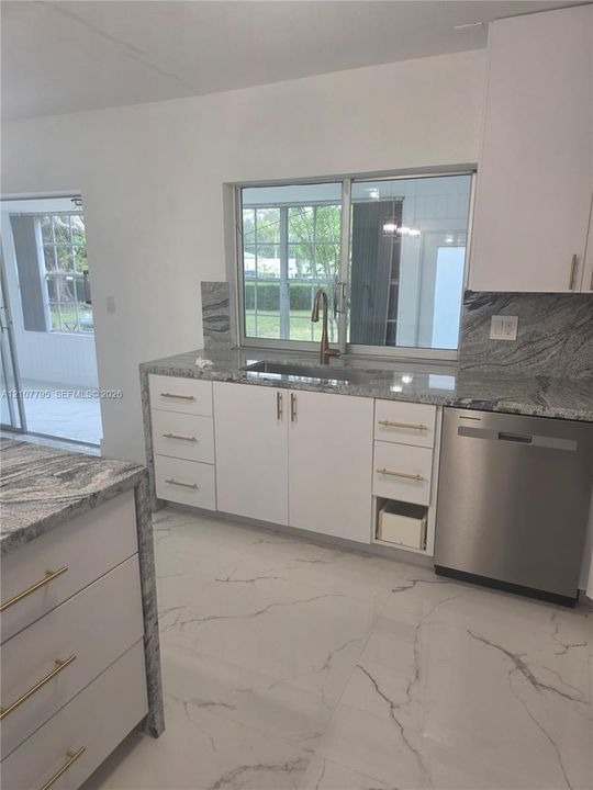 Kitchen featuring stone countertops, white cabinetry with metallic hardware, stainless steel dishwasher, undermount sink, and large-format flooring