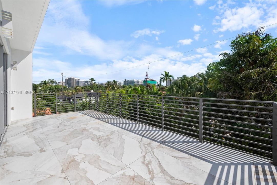 Expansive covered balcony featuring large-format stone-patterned tile flooring and a horizontal metal slat railing
