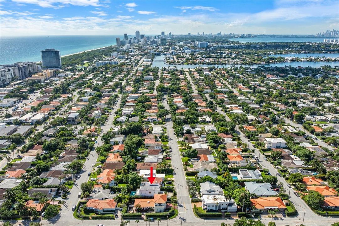 Aerial perspective showcasing a residential property with a swimming pool and multi-level roofline, situated within a coastal neighborhood near urban infrastructure and the shoreline