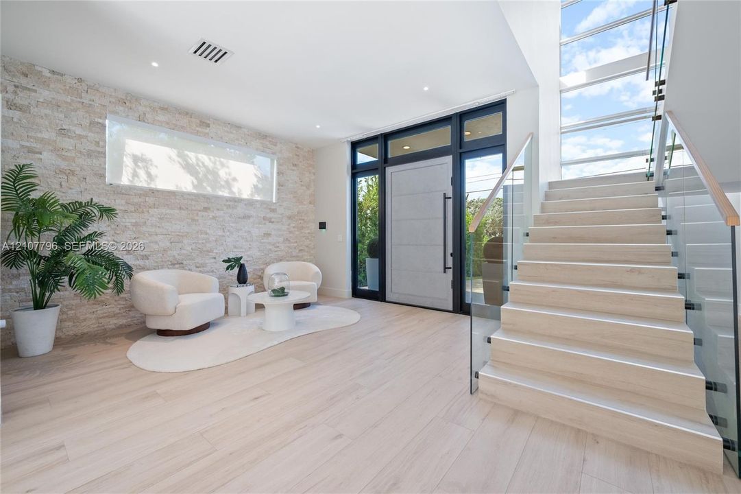 Entryway featuring a textured stone accent wall, light wood-finish flooring, a contemporary door with matte black hardware, and a staircase with glass railings and wood treads