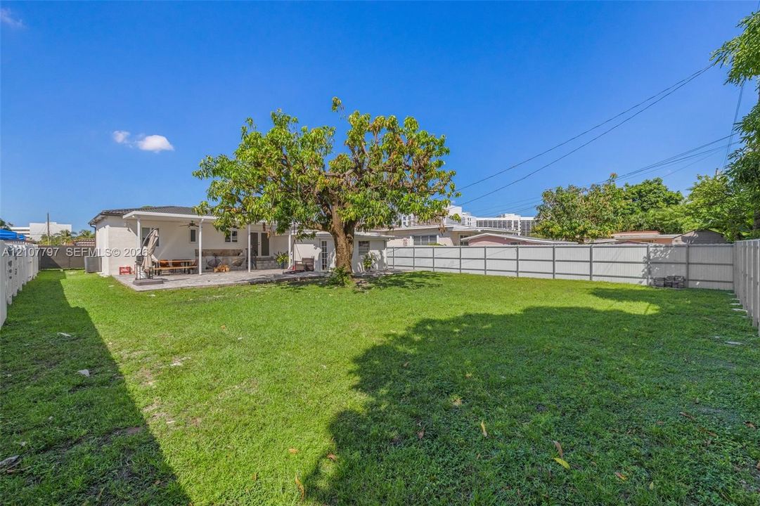Expansive backyard featuring a large grass lawn, a covered concrete patio, a mature shade tree, and perimeter fencing