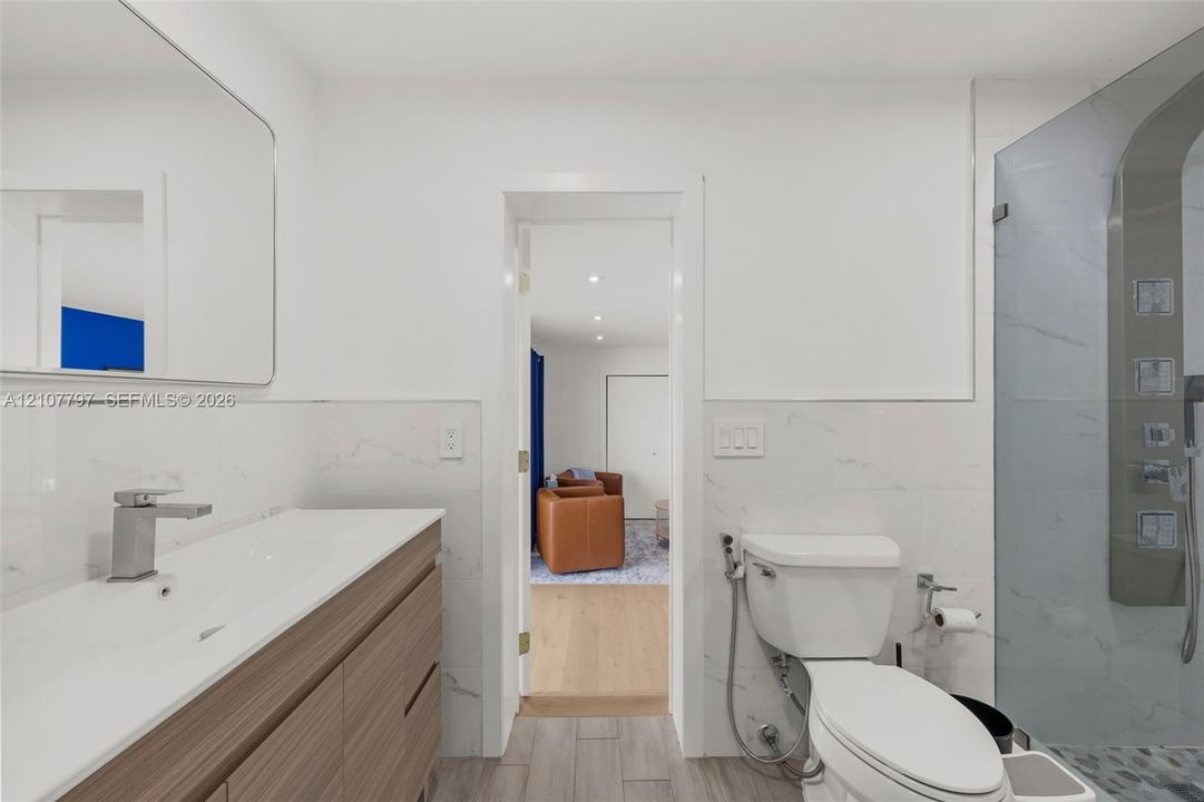 Bathroom featuring a wood-finish floating vanity with an integrated basin, wall-to-wall mirror, tiled flooring, and a walk-in shower with a glass enclosure and multi-head shower system