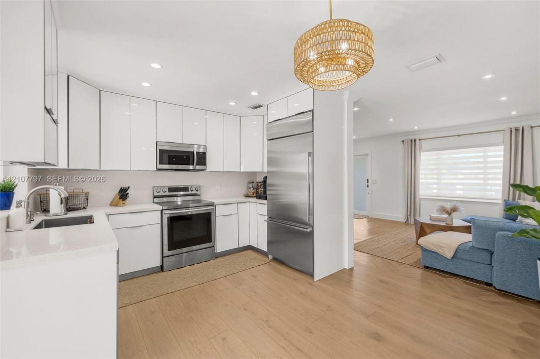 Kitchen featuring gloss-finish cabinetry, stainless steel appliances, light-toned stone countertops, wood-finish flooring, and a textured pendant light fixture