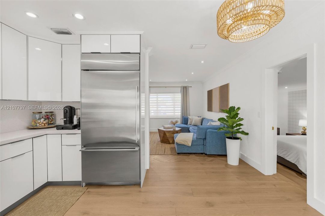 Kitchen featuring high-gloss white cabinetry, integrated stainless steel refrigerator, solid-surface countertops, recessed lighting, and wood-finish flooring