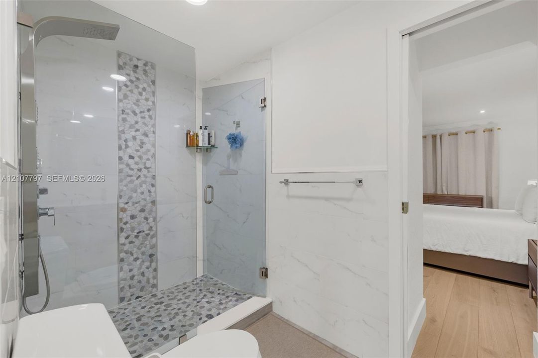 Walk-in shower featuring glass enclosure, stone-tiled floor, rainfall showerhead, and wall-mounted stainless steel fixtures