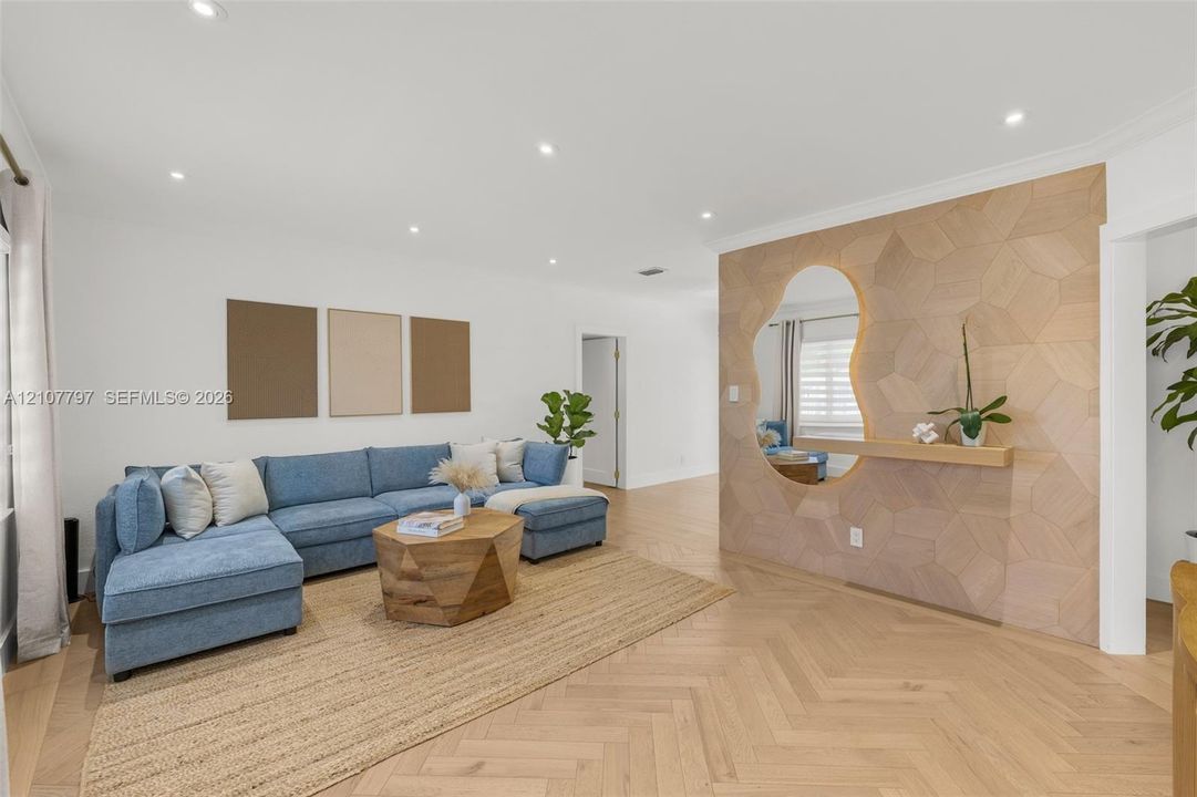 Herringbone wood-finish flooring, custom geometric wood-paneled accent wall, built-in floating shelf, organic-shaped wall mirror, and recessed lighting