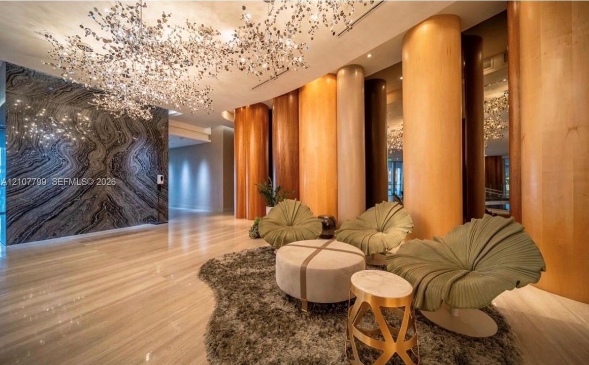Large-scale sculptural chandelier, full-height decorative wood-paneled pillars, polished stone flooring, and expansive accent wall featuring dramatic natural veining