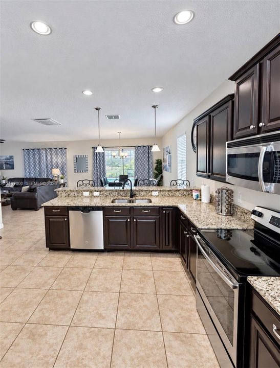 Kitchen featuring dark cabinetry, stone-finish countertops, stainless steel appliances, tile flooring, and recessed lighting