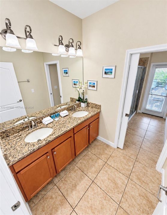Dual-sink vanity with natural stone countertops, tile flooring, and integrated wall-mounted lighting