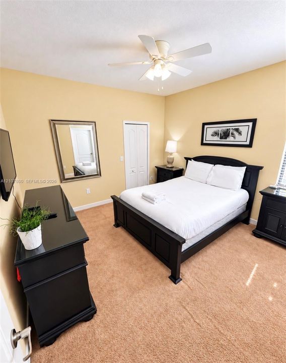 Bedroom featuring neutral carpeting, a ceiling-mounted light fixture with a central fan, and a built-in closet with double doors