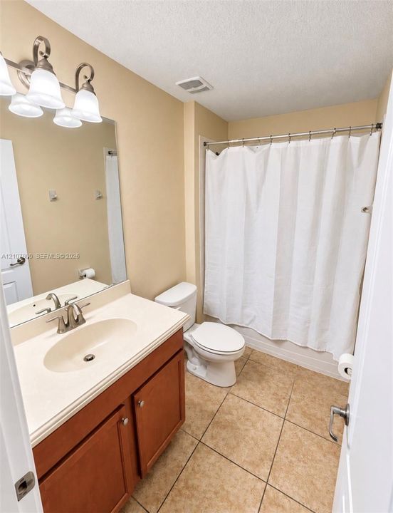 Bathroom featuring a wood-toned vanity with an integrated sink, neutral stone-finish countertop, tiled flooring, and multi-bulb vanity lighting