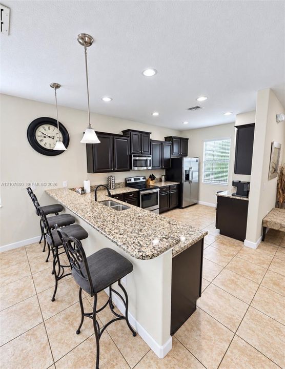 Kitchen featuring dark cabinetry, expansive stone-finish countertops, stainless steel appliances, dual pendant lighting, and ceramic tile flooring