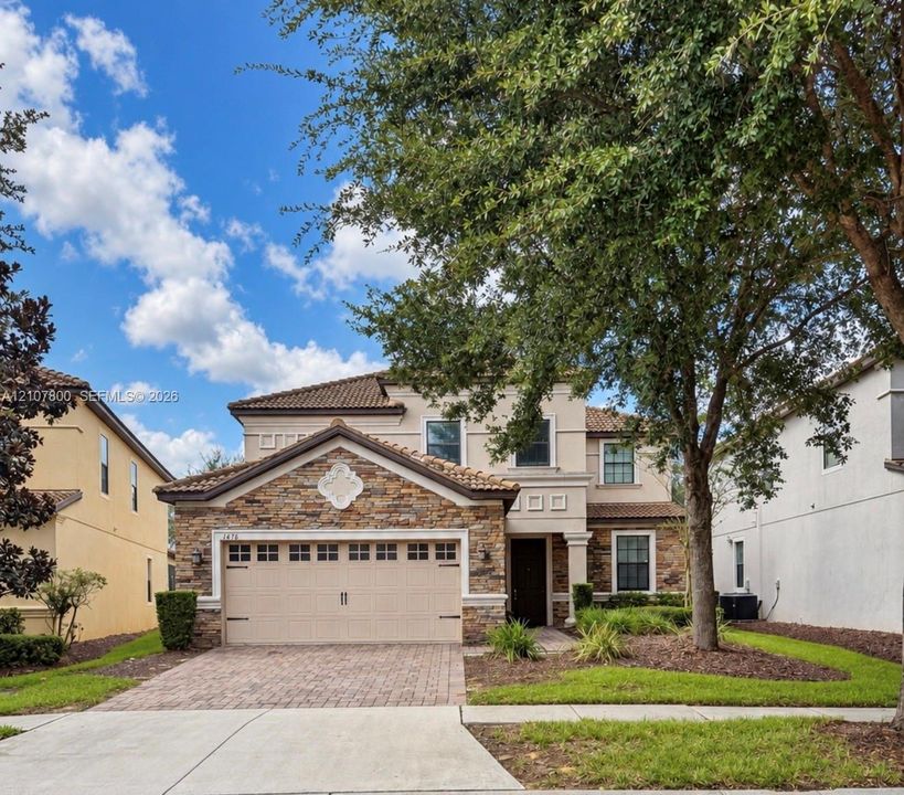 Two-story exterior featuring a stone veneer facade, tile roofing, an attached multi-car garage, and a brick-paver driveway