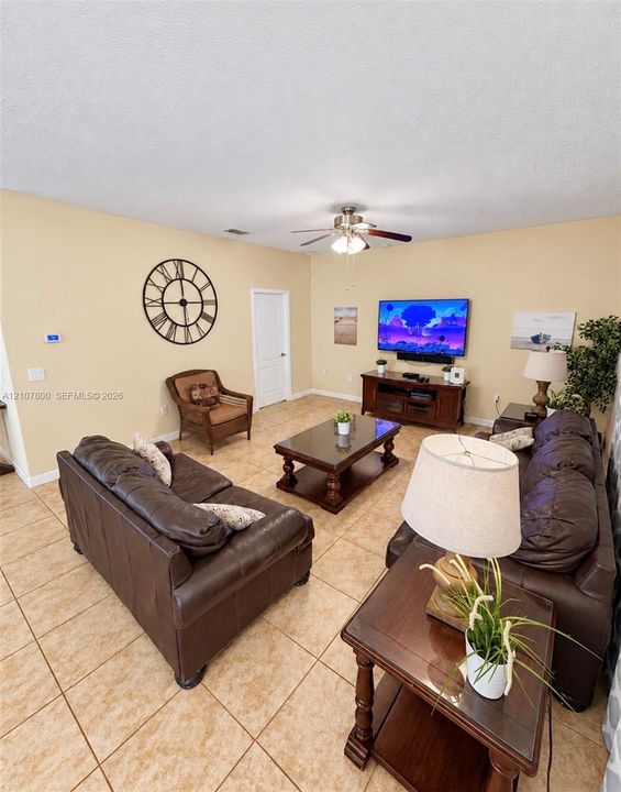 Neutral-toned living space featuring large-format ceramic tile flooring, a central ceiling fan with integrated lighting, and a solid-core interior door